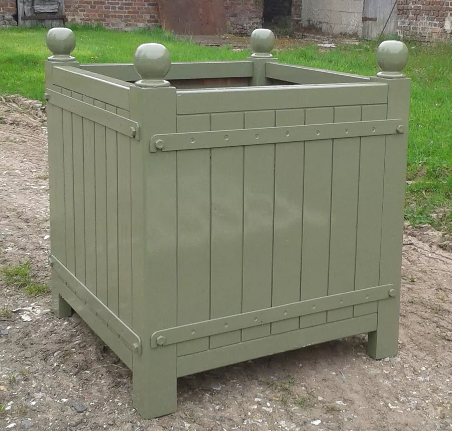 Orangerie Pflanzkübel aus lackiertem Akazienholz steht auf einem gepflasterten Weg im Freien vor einer Wiese und einem Backsteingebäude