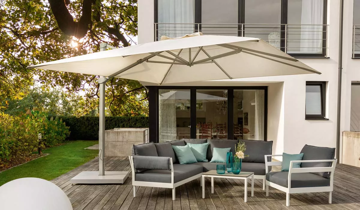 Weißer Weishäupl Cantilever Sonnenschirm auf einer Holzterrasse vor einem modernen Haus, umgeben von grauen Gartenmöbeln.
