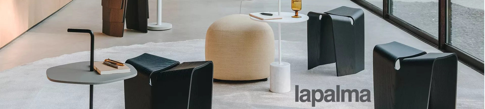 Lapalma Möbel in modernem Showroom mit schwarzem Hocker, weißem Tisch und beigem Pouf auf grauem Teppichboden.
