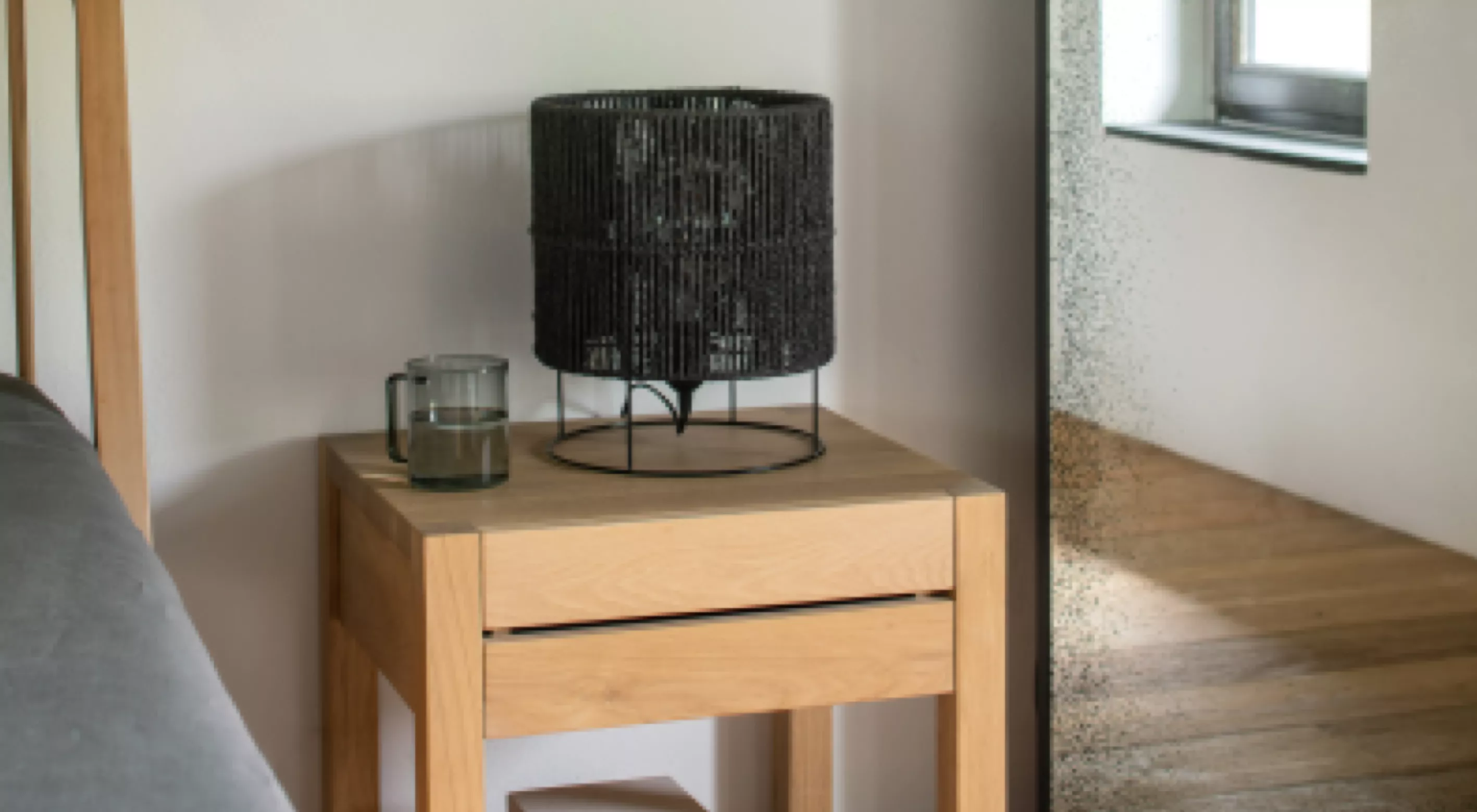 Schwarze Tischlampe auf hellem Holztisch neben großem Spiegel in modernem Schlafzimmer mit Tageslicht.