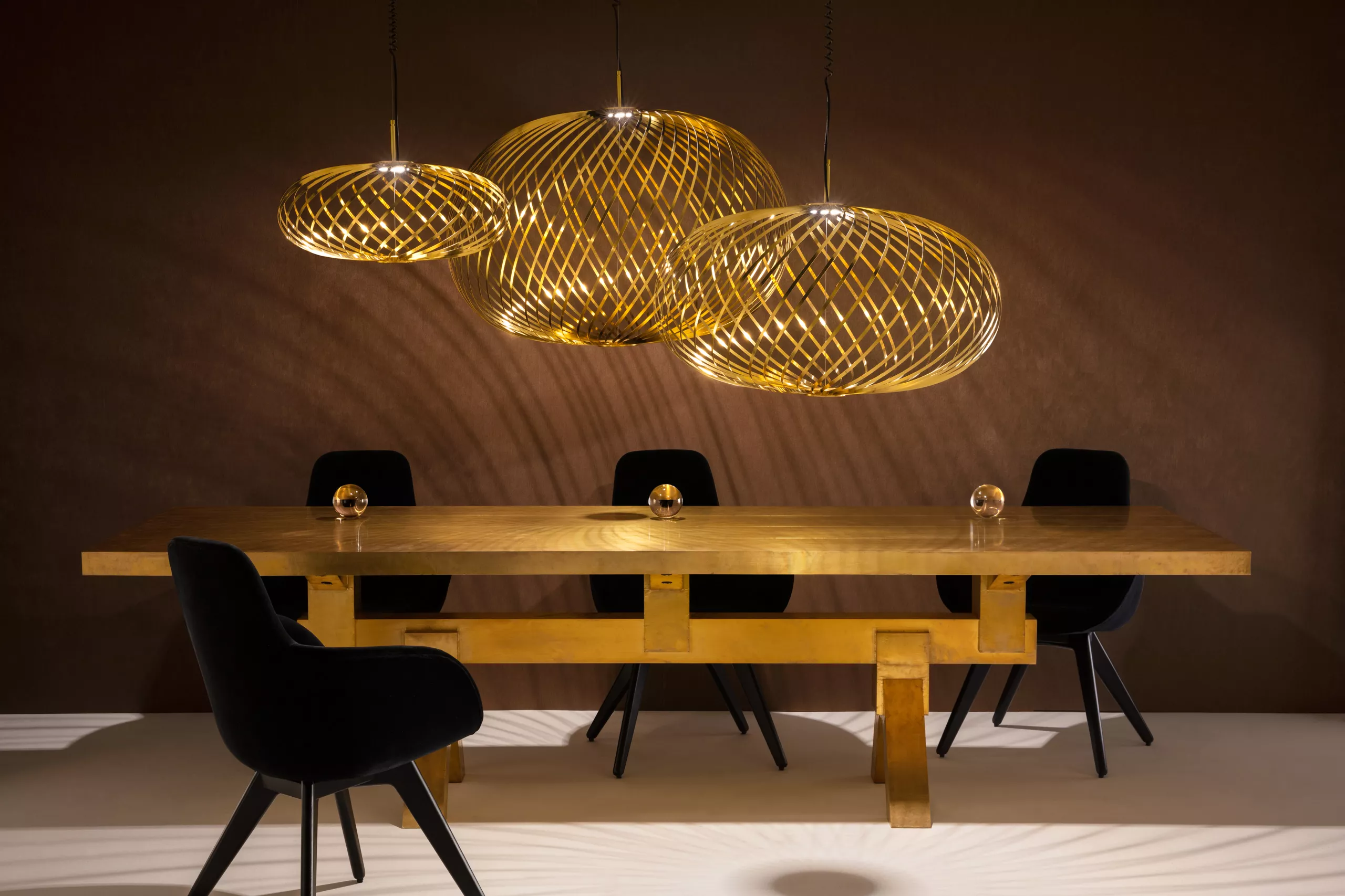 Tom Dixon Spring Brass Small Pendelleuchte in einem modernen Esszimmer mit dunklen Wänden und einem Holztisch, stimmungsvolle Beleuchtung.