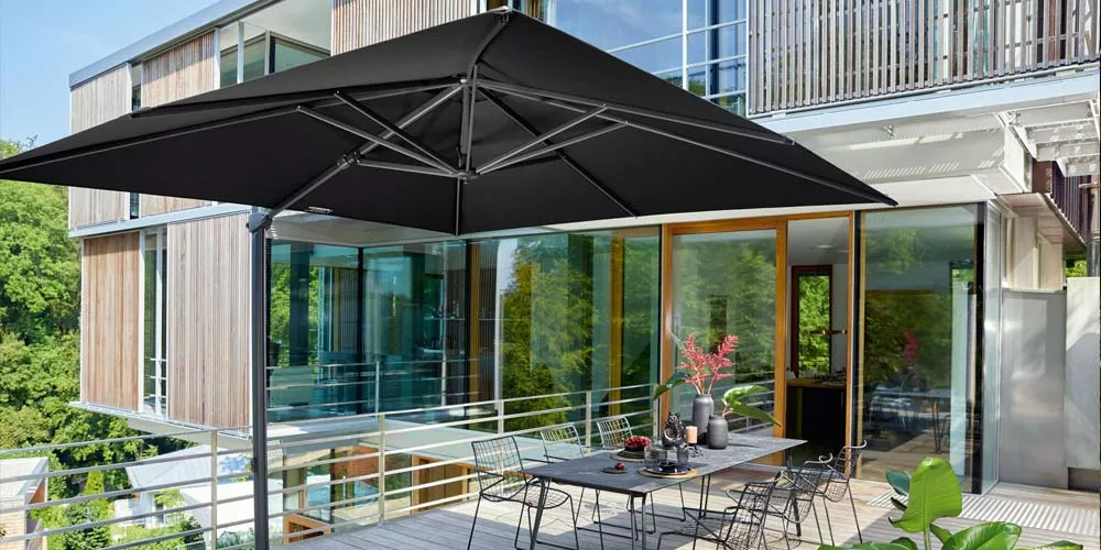 Weishäupl Freiarmschirm in Schwarz auf einer modernen Terrasse vor einem verglasten Gebäude, umgeben von grüner Natur.