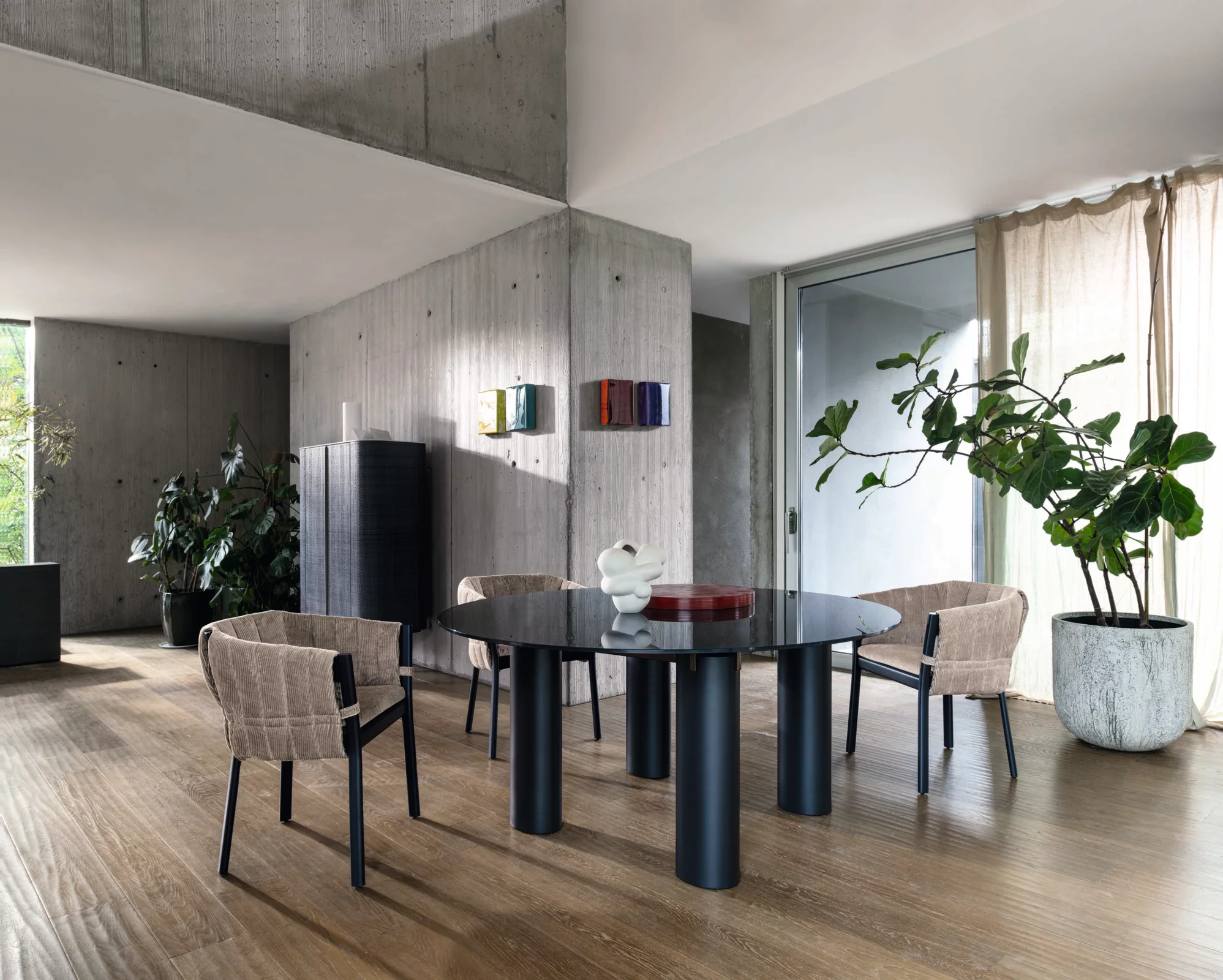 Gervasoni Moodbild zeigt einen modernen Essbereich mit einem runden schwarzen Tisch und vier beigen Stühlen in einem stilvollen Raum mit Pflanzen.