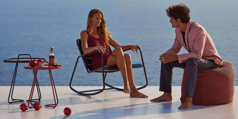 Zwei Personen entspannen auf der Cane-line Copenhagen Loungegruppe in Schwarz und Rot auf einer Terrasse mit Meerblick.