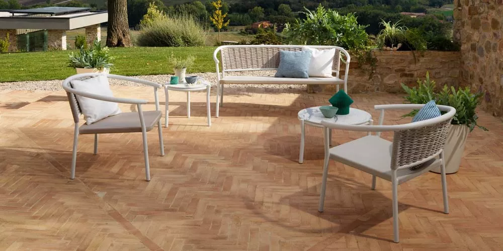 Roberti Lipari Outdoor-Loungegruppe in Beige auf einer Terrasse mit Natursteinmauer und Blick auf einen grünen Garten.