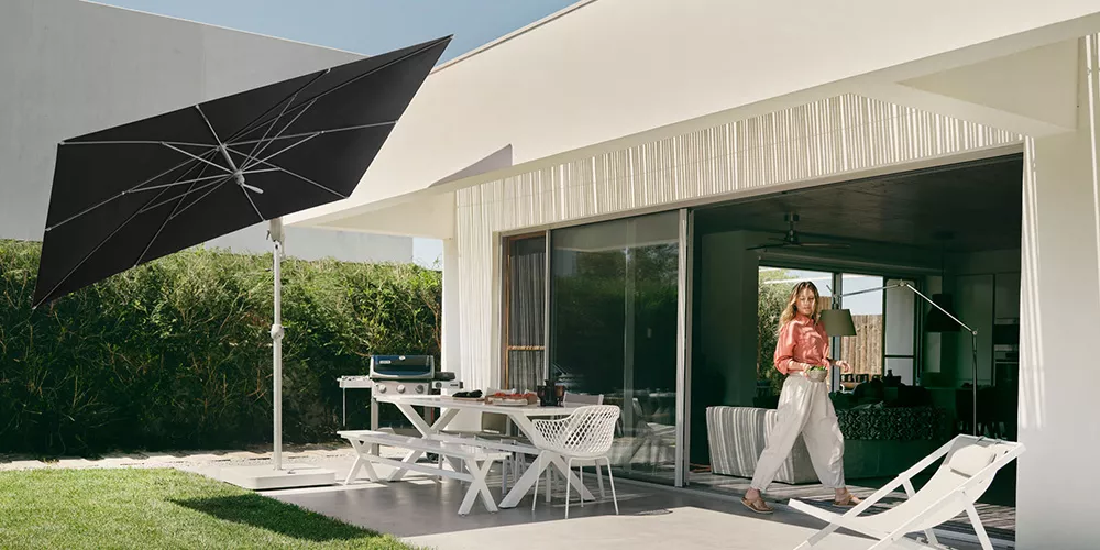 Glatz Pendalex Sonnenschirm in Schwarz auf einer modernen Terrasse mit weißem Tisch und Stühlen, im Hintergrund ein Haus mit Glasfront.