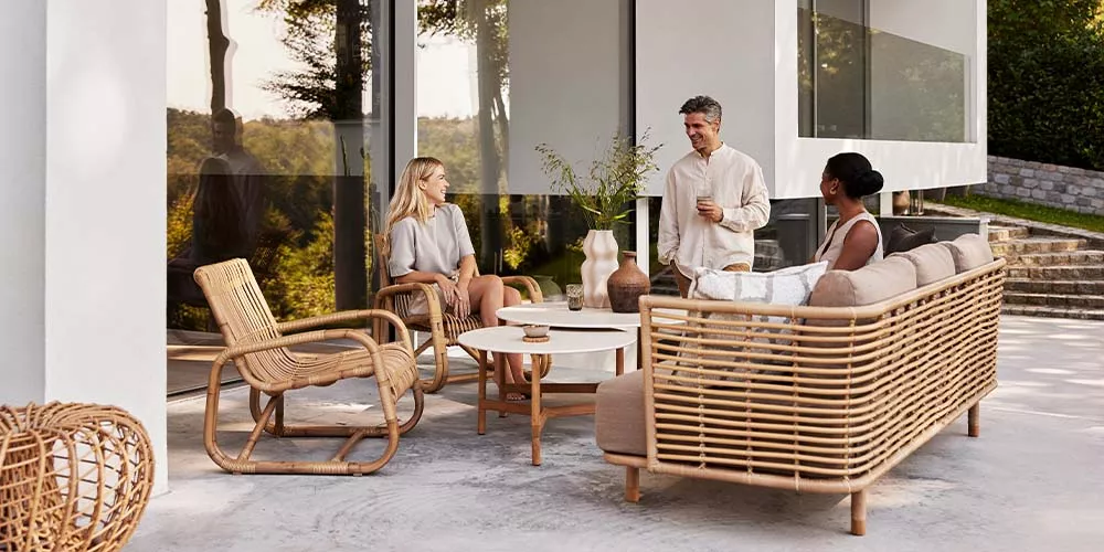 Cane-line Sense Kollektion in Naturtönen, bestehend aus Sofa, Sessel und Tisch, auf einer Terrasse mit modernem Hintergrund.