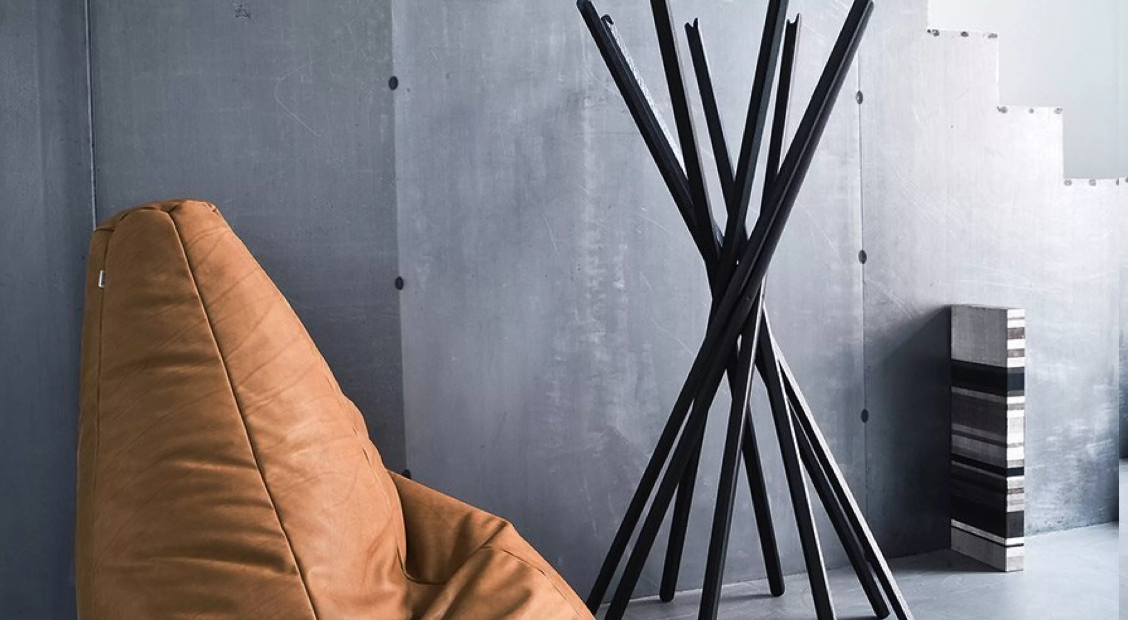 Brauner Ledersessel und schwarzer Sciangai-Kleiderständer von Zanotta vor einer grauen, industriellen Wand.