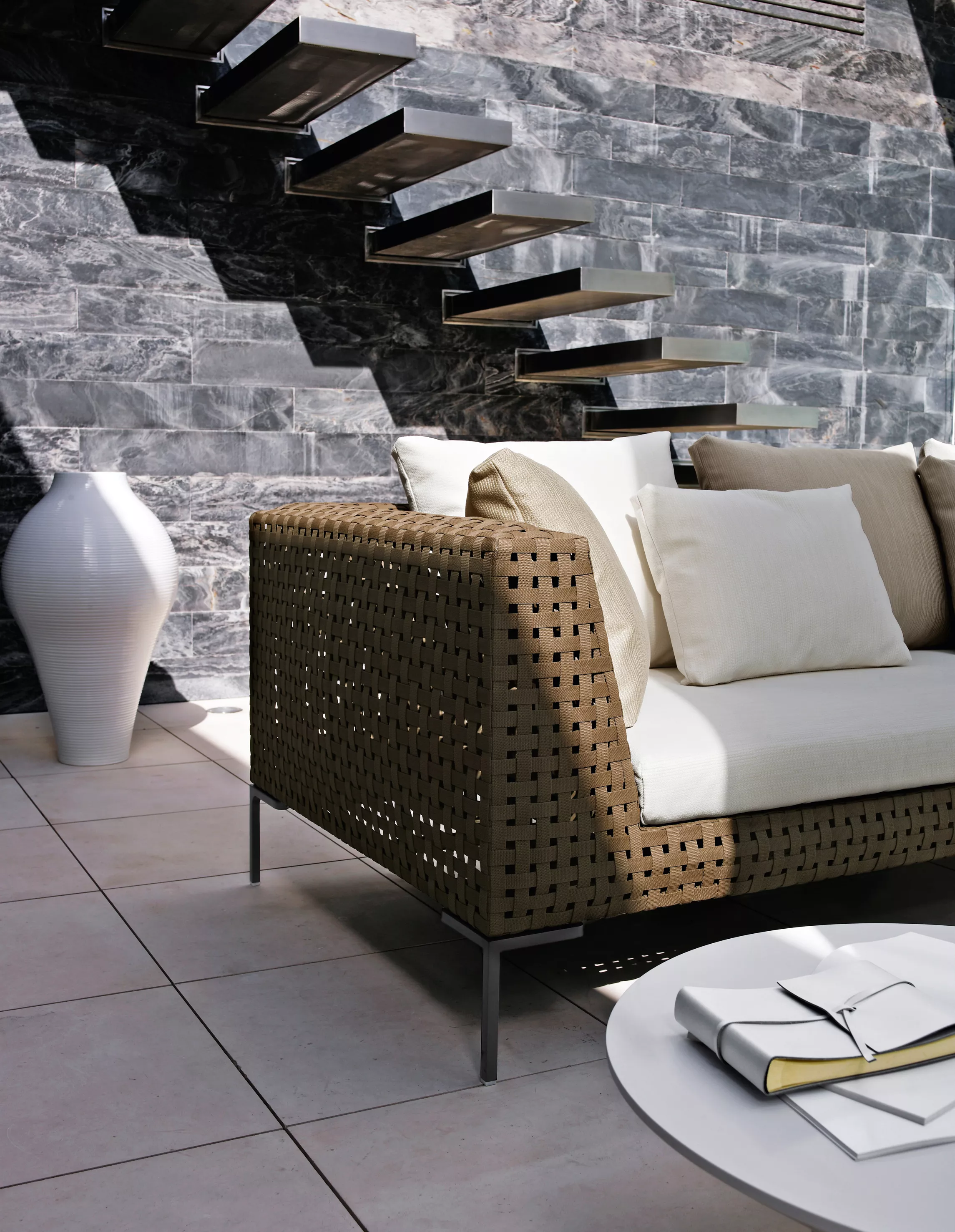 Charles Outdoor Sofa 234 cm von B&B Italia steht auf einer Terrasse neben einer weißen Vase und einem runden Tisch mit Büchern und Notizbuch
