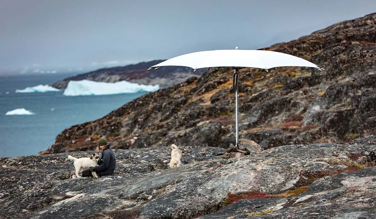 Ein weißer Ocean Master Crescendo Sonnenschirm steht auf felsigem Gelände mit Blick auf das Meer und Eisberge im Hintergrund.