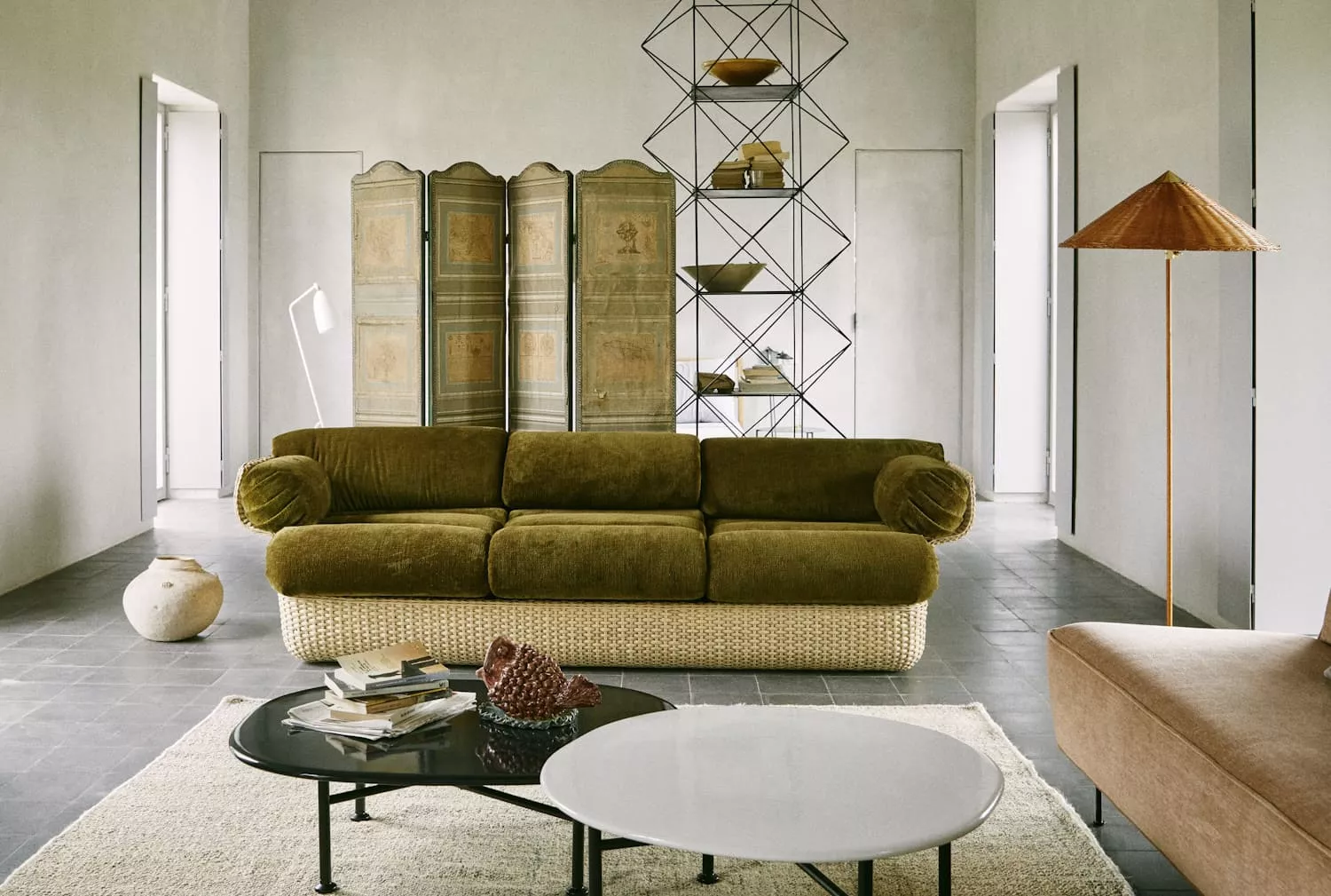 Ein Wohnzimmer mit einem grünen Gubi Sicilia Sofa einem Couchtisch und einem Raumteiler im Hintergrund