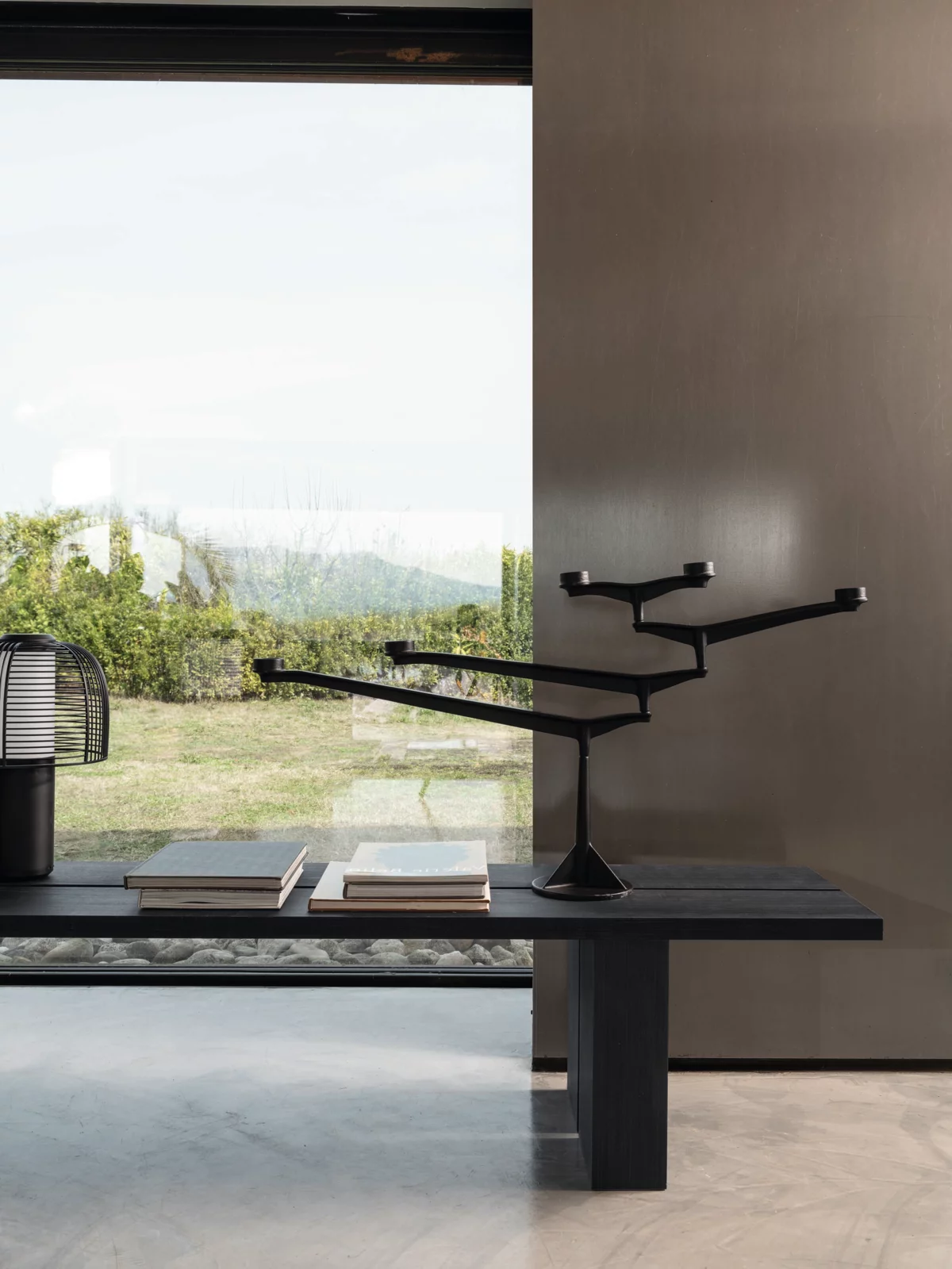 Gervasoni Leuchte Modell 100 in Schwarz auf einem Tisch neben Büchern und einer Lampe mit Blick auf einen Garten