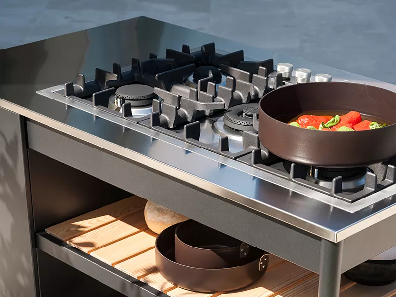 Roda Norma Küche in Schwarz mit Edelstahloberfläche, Gasherd und Pfanne, Detailansicht auf modernem, minimalistischem Hintergrund.