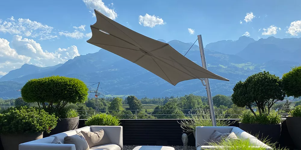 Sonnenschirm Glatz Spectra in Beige auf einer Terrasse mit Bergblick und weißen Loungemöbeln, stimmungsvolles Outdoor-Ambiente.