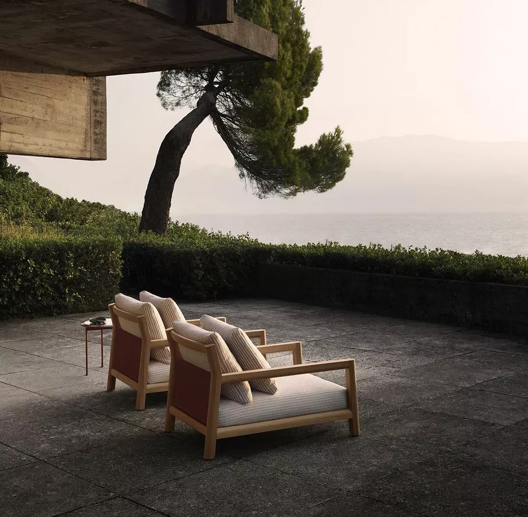 Zwei B&B Italia Pablo Outdoor Loungesessel stehen auf einer Terrasse mit Blick auf das Meer und einen Baum im Hintergrund
