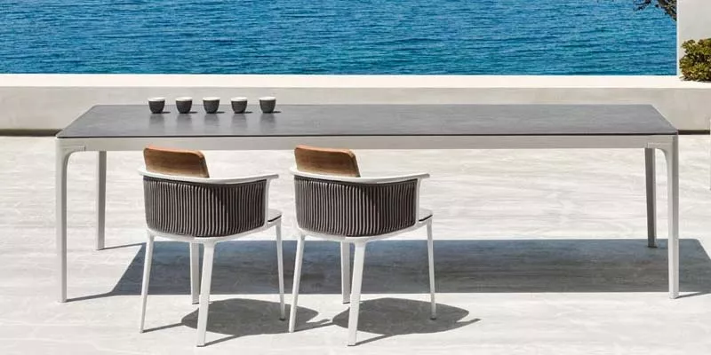 Ethimo Play Outdoor Loungegruppe in Grau auf einer Terrasse mit Meerblick, bestehend aus einem langen Tisch und zwei Stühlen.