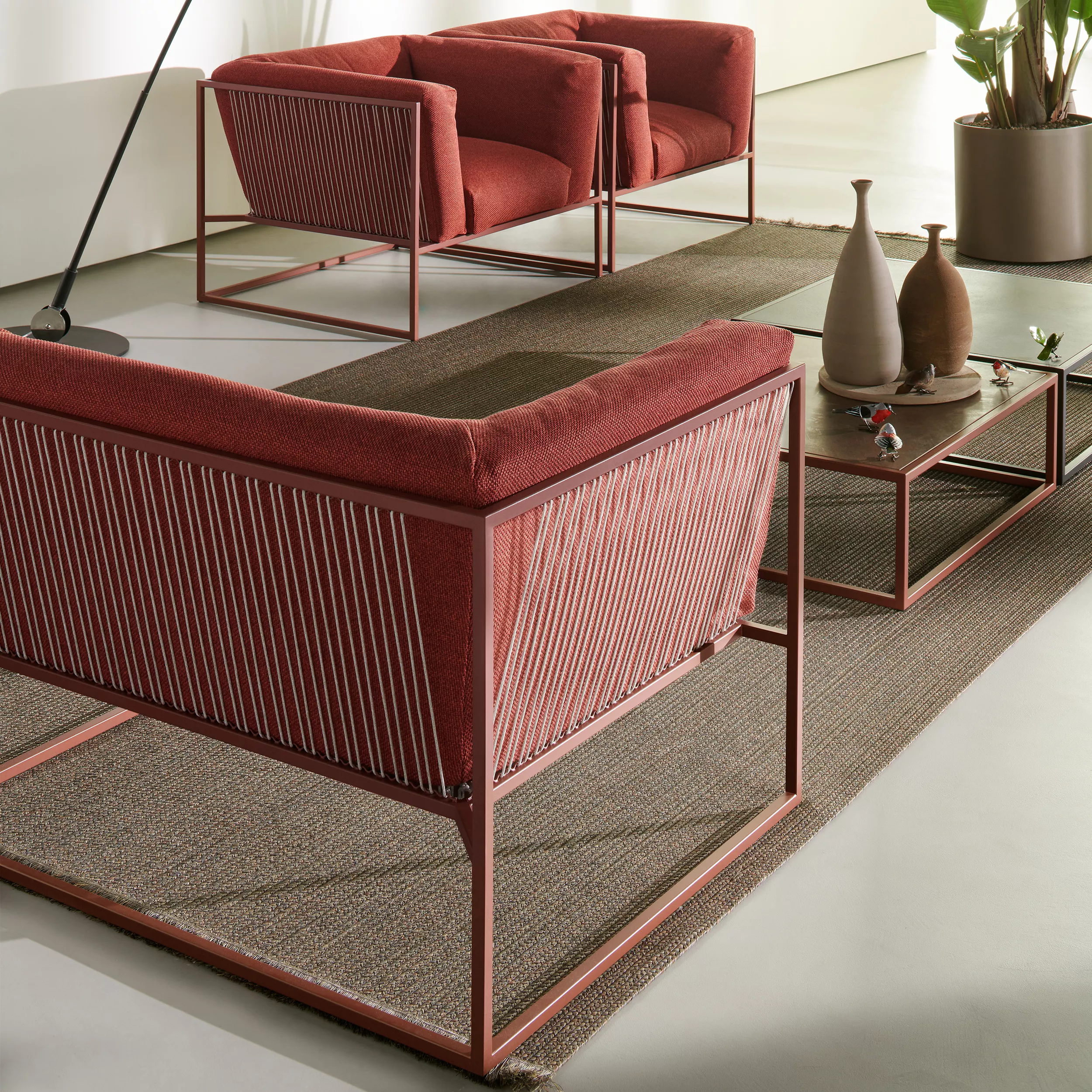 Zwei MDF Italia Arpa Loungesofas in Rot mit passendem Couchtisch und Dekoration in einem modernen Wohnzimmer mit Pflanzen und Teppich.