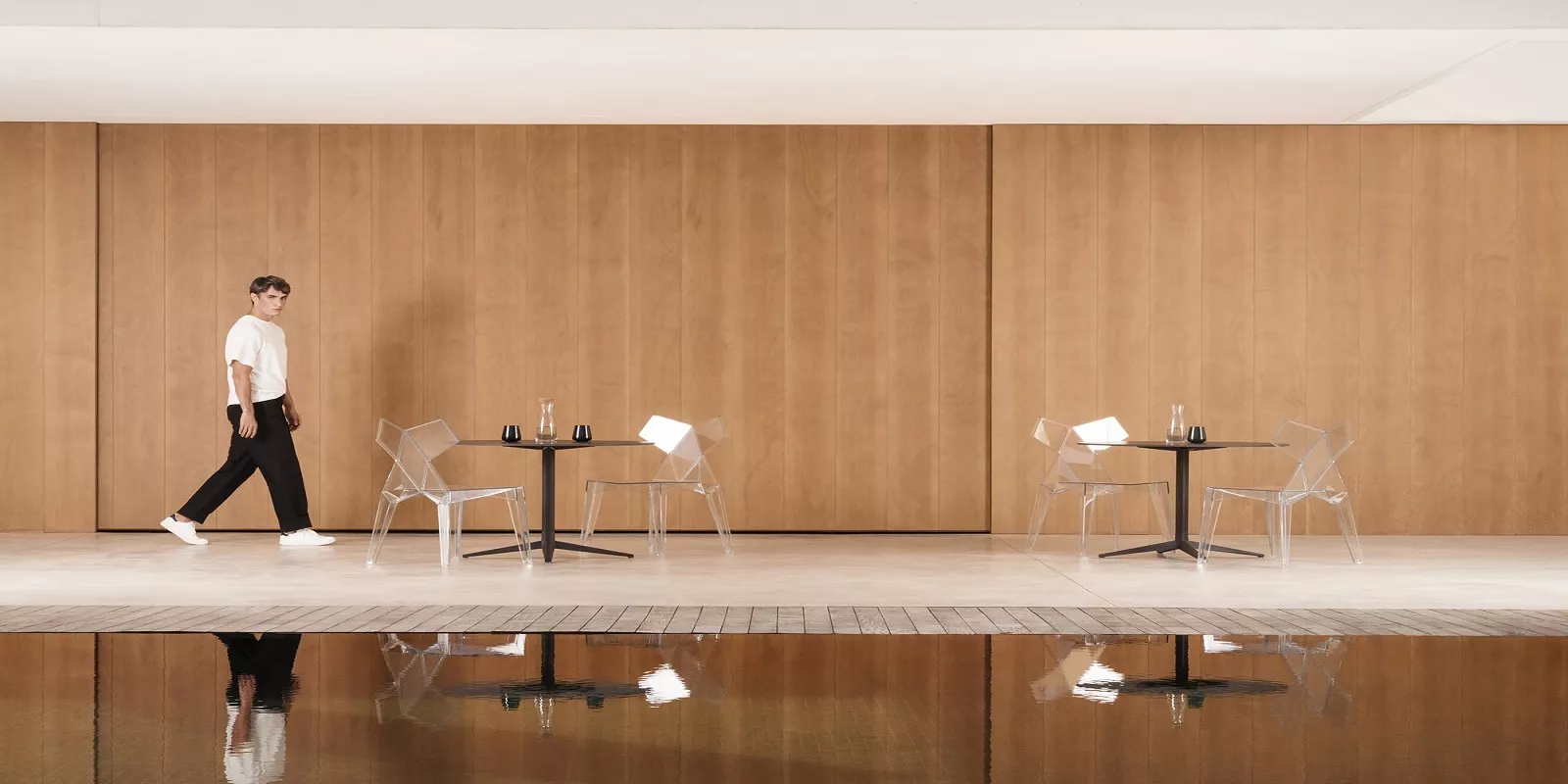 Ein Mann geht an einem Pool entlang, vorbei an Vondom Kimono Stühlen von Ramon Esteve, auf einer Terrasse mit Holzwand im Hintergrund.