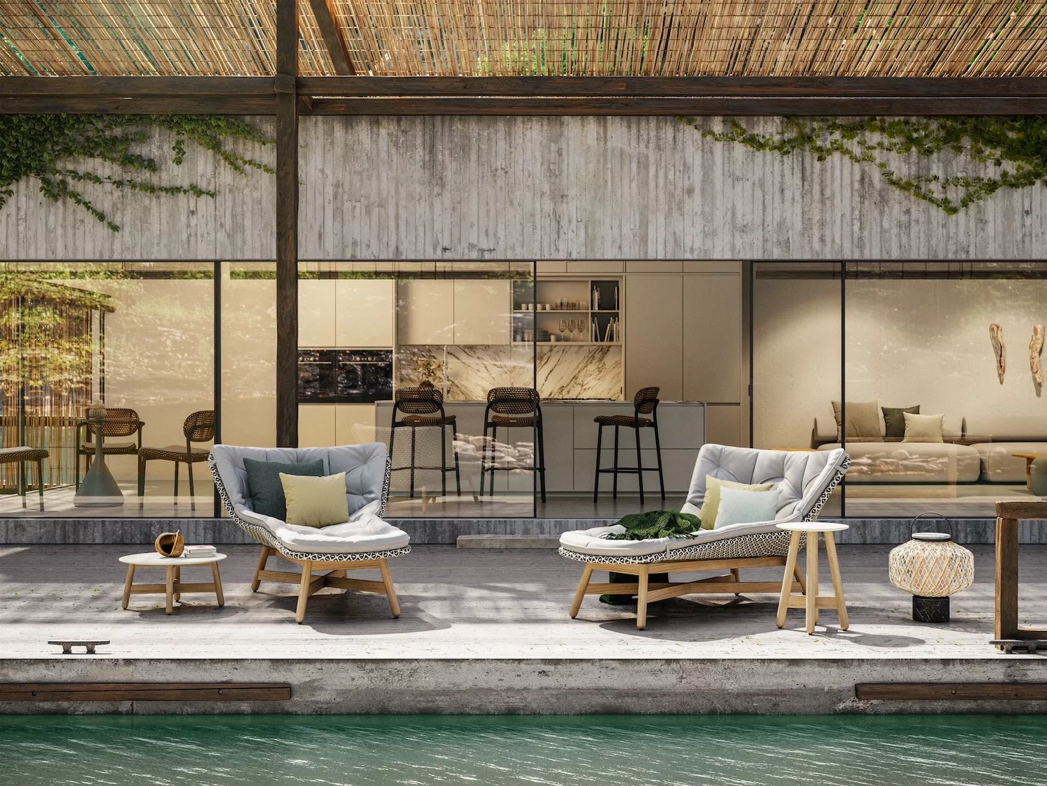 Zwei Dedon Mbrace Gartenliegen mit Kissen und Beistelltischen stehen auf einer Terrasse vor einem modernen Haus mit Glasfront und Blick auf einen Pool