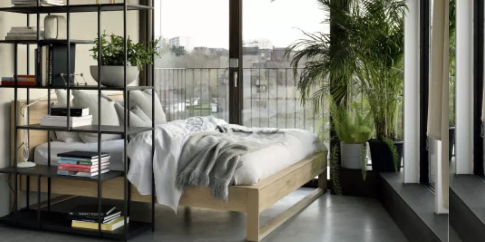 Gemütliches Schlafzimmer mit Holzbett, grauer Decke und Pflanzen, Blick auf Balkon durch große Fenster, modernes und helles Ambiente.