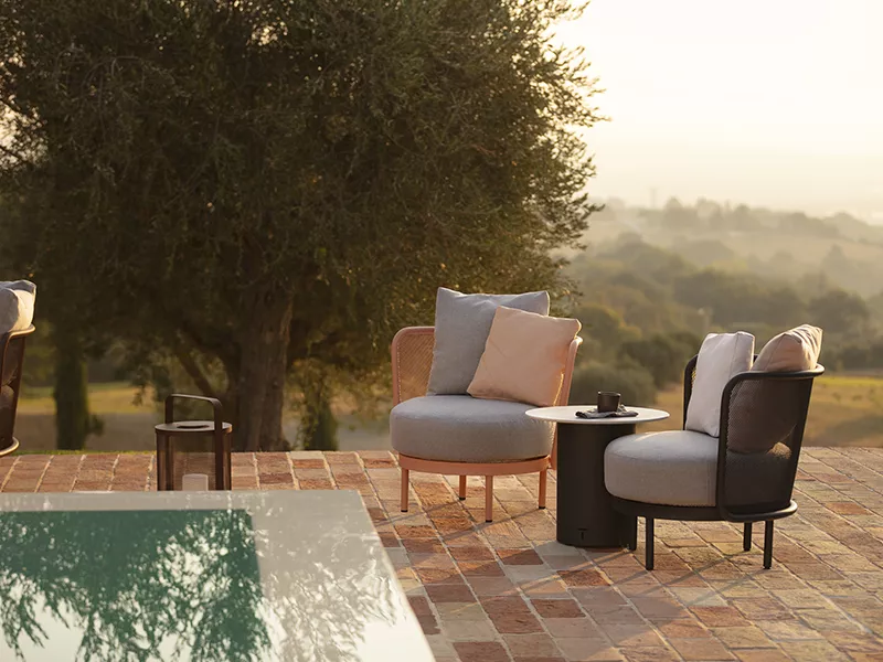 Zwei Todus Baza Loungesessel in Grau und Beige stehen auf einer Terrasse mit Blick auf eine Landschaft bei Sonnenuntergang.