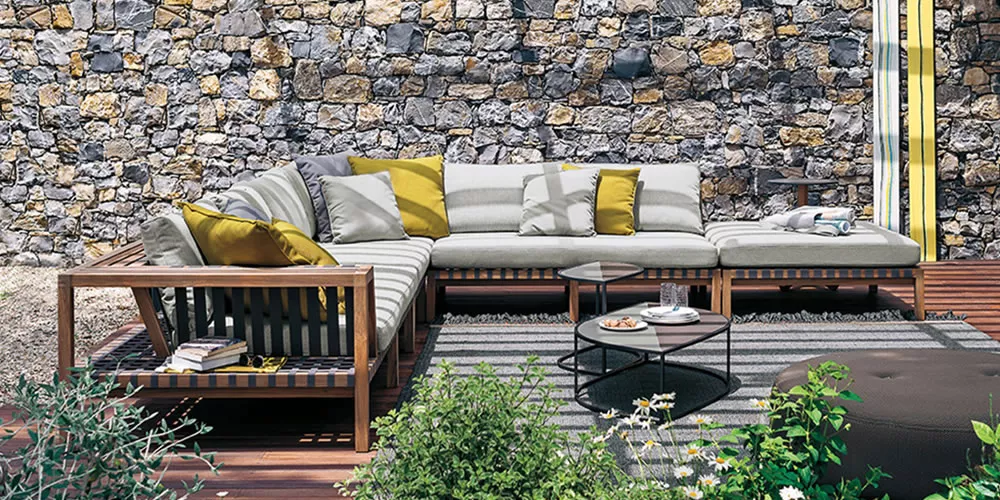 Roda Kollektion Network Lounge in Grau und Holz auf einer Terrasse mit Steinmauer im Hintergrund, umgeben von Pflanzen.