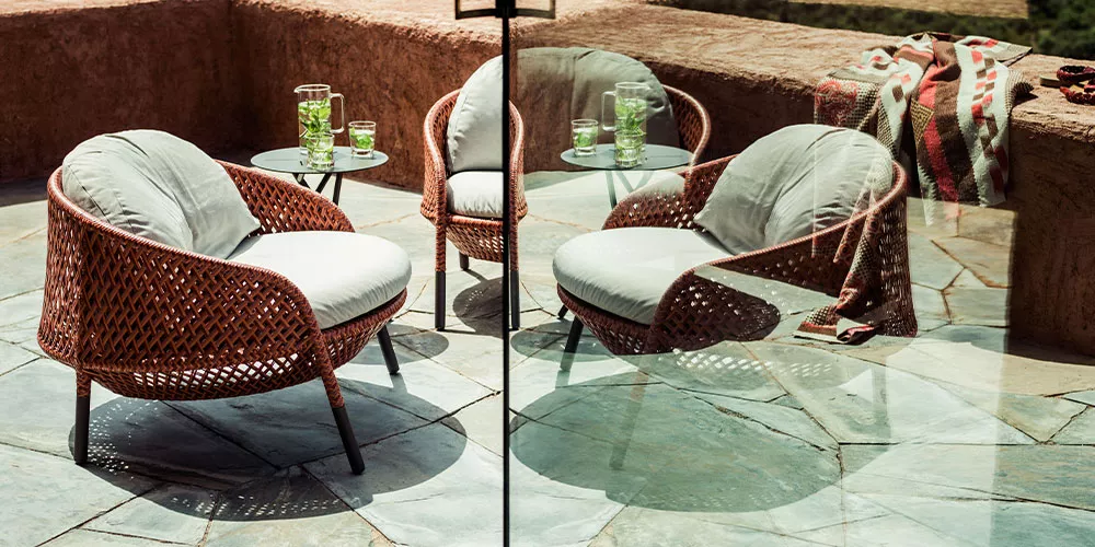 Drei Dedon Andah Sessel mit weißen Kissen und zwei Beistelltische mit Getränken auf einer Terrasse bei sonnigem Wetter.