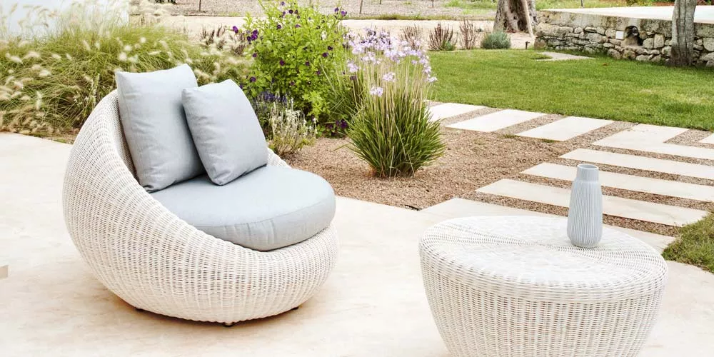 Weiße Point Bubble Outdoor-Loungegruppe mit rundem Sessel und Tisch auf einer Terrasse, umgeben von grünem Garten.