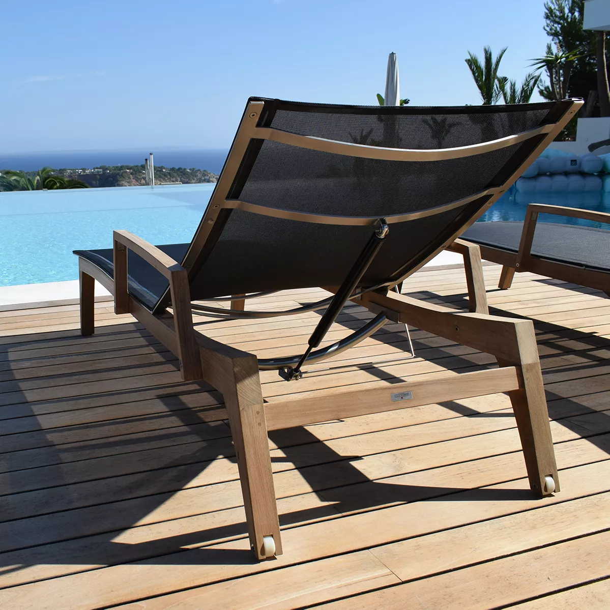 Sonnenliege Muse von Royal Mirage in Schwarz auf Holzterrasse mit Meerblick im Hintergrund.