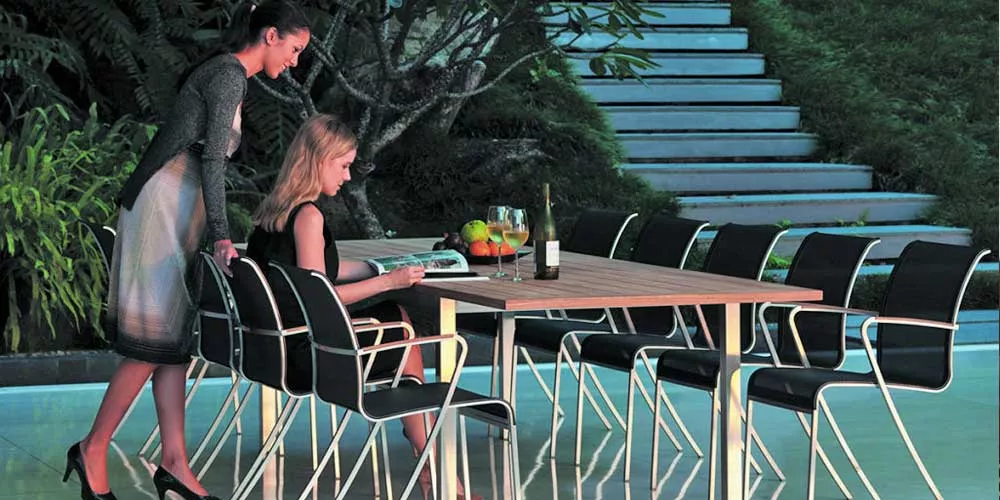 Zwei Frauen sitzen an einem Royal Botania Red Label Taboela Essgruppe im Garten, umgeben von Pflanzen und Treppen im Hintergrund.