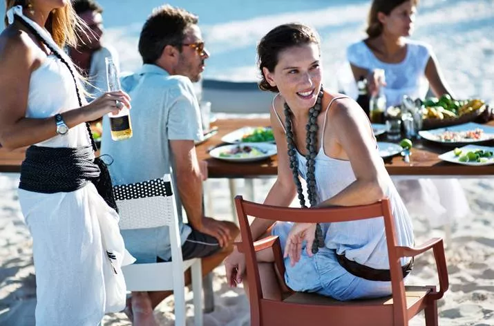 Menschen sitzen und stehen um einen gedeckten Tisch am Strand und genießen eine Mahlzeit im Freien auf Dedon Play Essstühlen