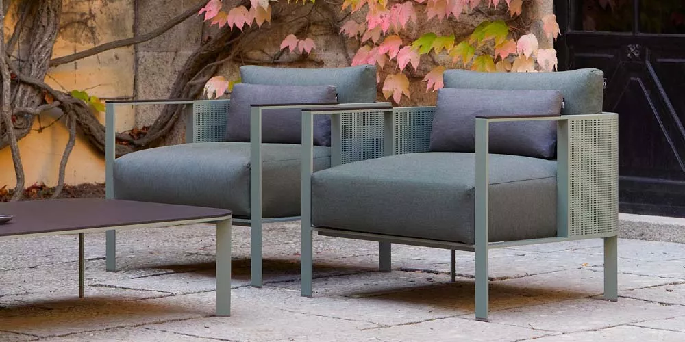 Zwei grüne Gandia Blasco Solanas Sessel auf einer Steinterrasse vor einer mit Efeu bewachsenen Wand.