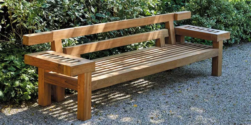 Royal Botania Nara Gartenbank aus Holz auf Kiesweg vor grüner Hecke, stimmungsvolles Gartenbild.