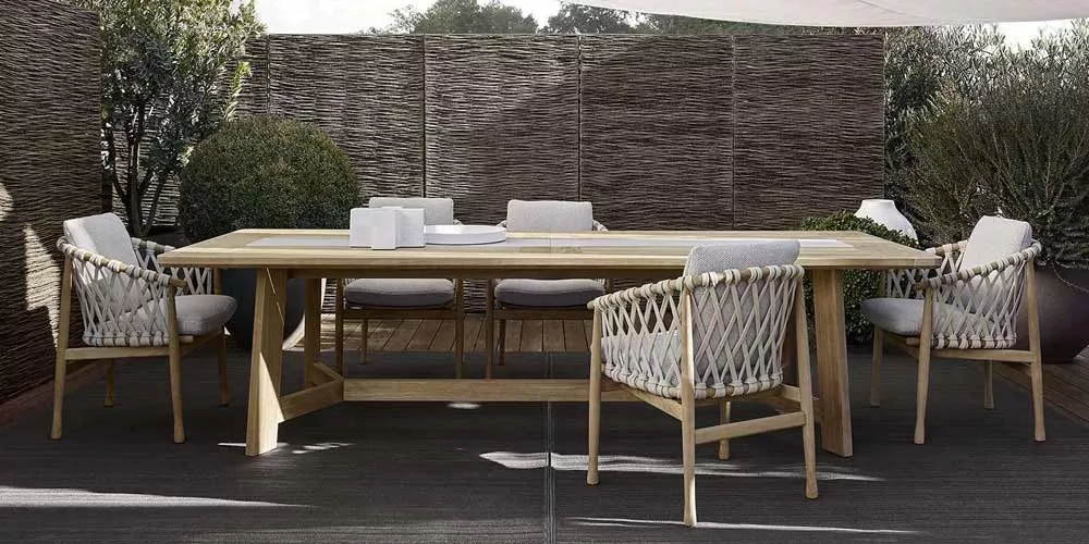 Essgruppe BeB Italia Ginestra bestehend aus einem großen Holztisch und sechs geflochtenen Stühlen in einem stilvollen Gartenambiente