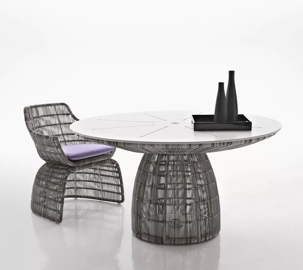 B&B Italia Crinoline Outdoor Armlehnstuhl mit Polyethylenfasergeflecht neben einem runden Tisch mit Dekoration auf weißem Hintergrund