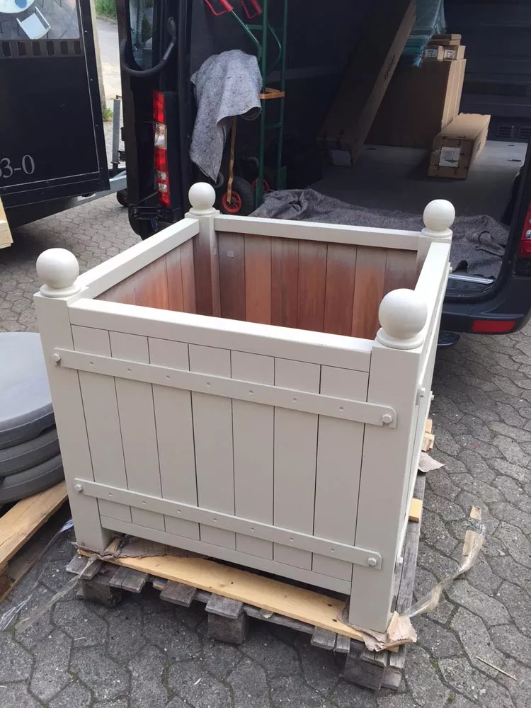 Orangerie Pflanzkübel aus lackiertem Akazienholz steht auf einer Palette vor einem Lieferwagen im Freien