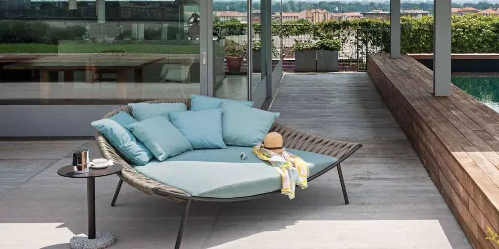 Roda Bernardo Beistelltisch in Dunkelbraun neben einer modernen, runden Outdoor-Liege mit blauen Kissen auf einer Terrasse.