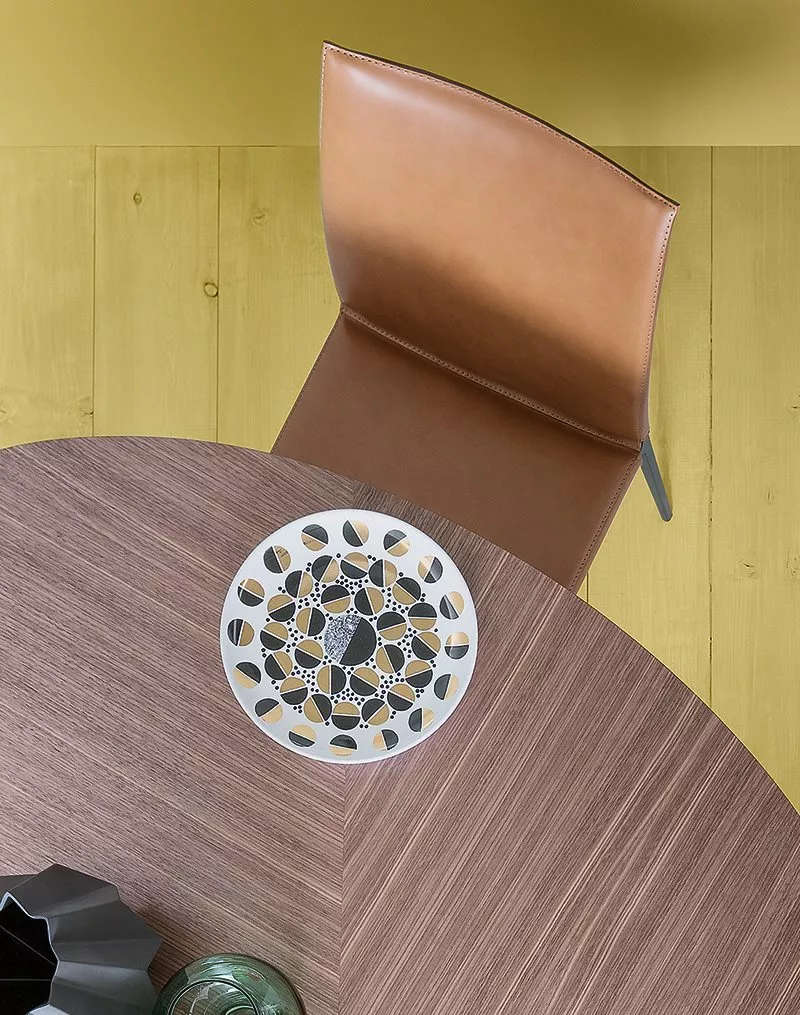 Ein brauner Zanotta Lia Stuhl steht an einem runden Holztisch auf dem ein dekorativer Teller und eine Vase stehen Moodbild von oben.