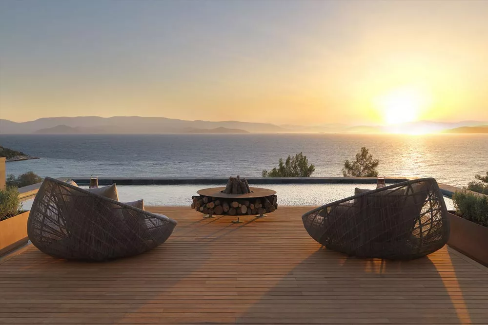 Zwei moderne Loungesessel und ein AK47 Zero Feuerstelle 145 cm Gartenkamin auf einer Terrasse mit Meerblick bei Sonnenuntergang