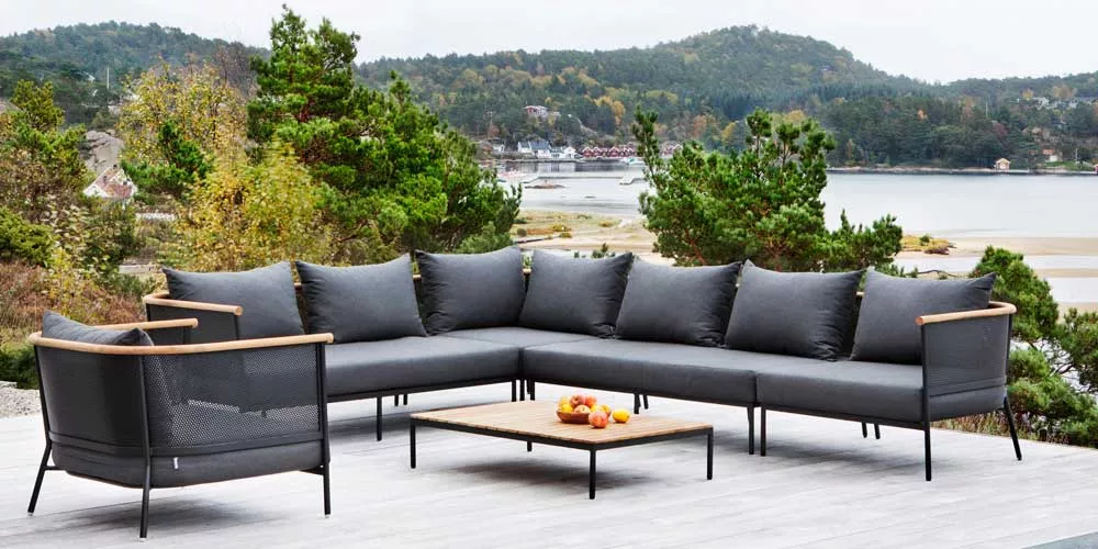 Oasiq Riad Loungegruppe in Anthrazit auf einer Terrasse mit Seeblick, bestehend aus Ecksofa und Tisch, umgeben von grüner Natur.