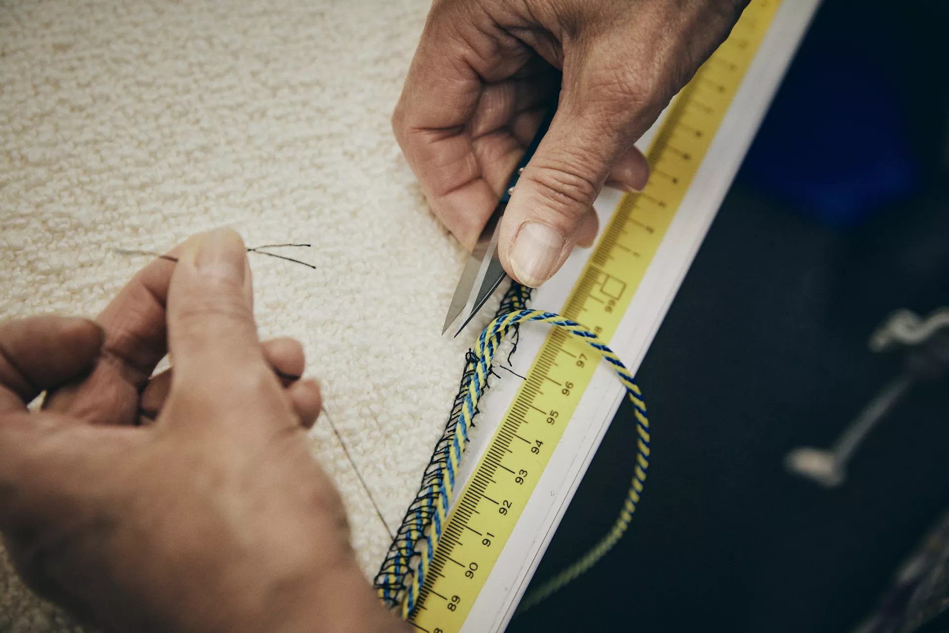Hände schneiden bunte Kordel auf gelbem Maßband, Nahaufnahme, Hintergrund unscharf.