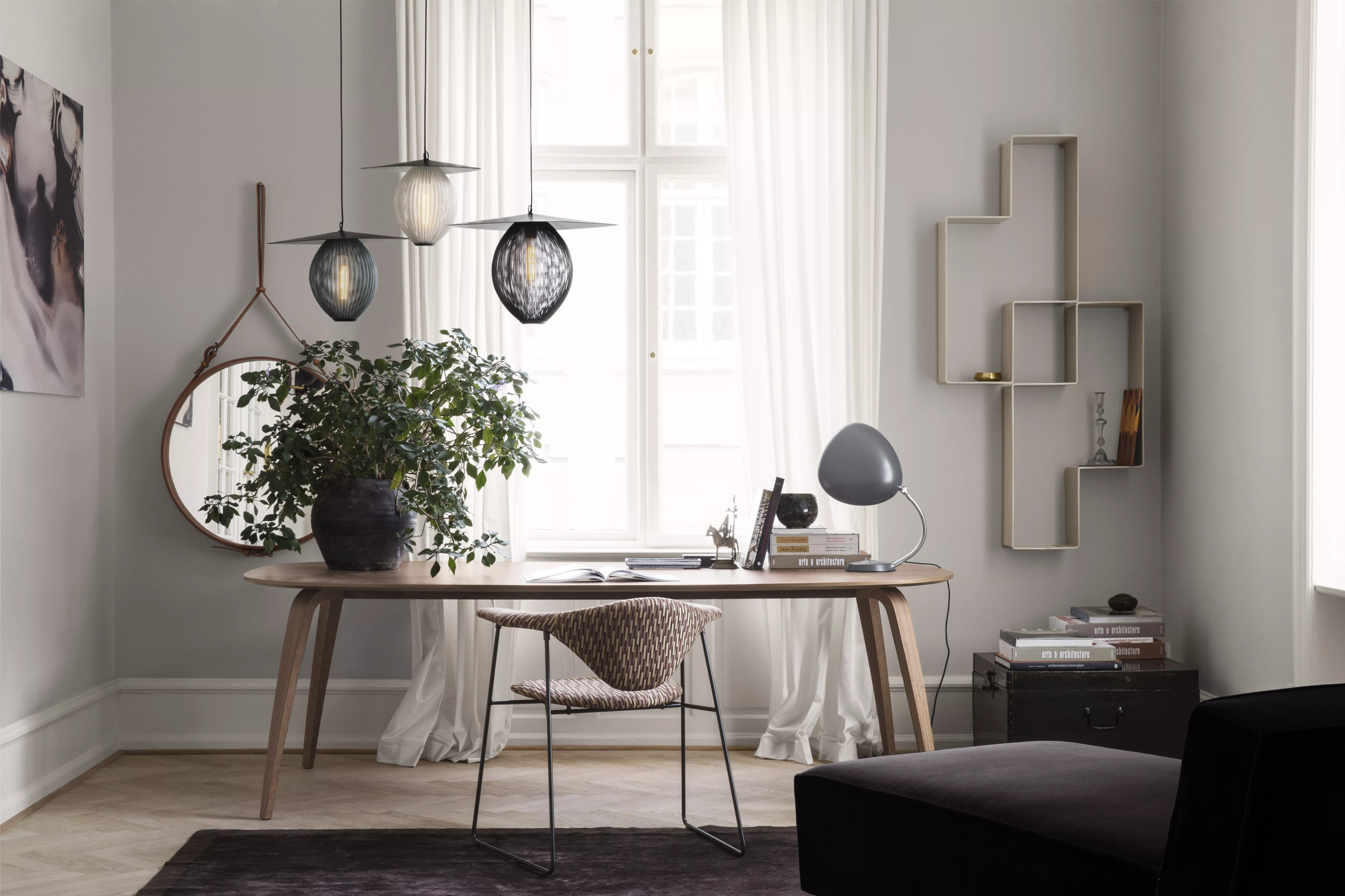 Ein stilvoll eingerichtetes Wohnzimmer mit GUBI Dining Table Elliptical und Masculo Dining Chair Sledge Base sowie Adnet Wall Mirror Circular und Pflanzen.