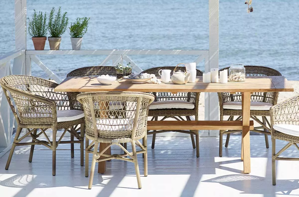 Sika Design Colonial Essgruppe in Naturtönen auf einer Terrasse mit Meerblick, bestehend aus einem Holztisch und sechs geflochtenen Stühlen.