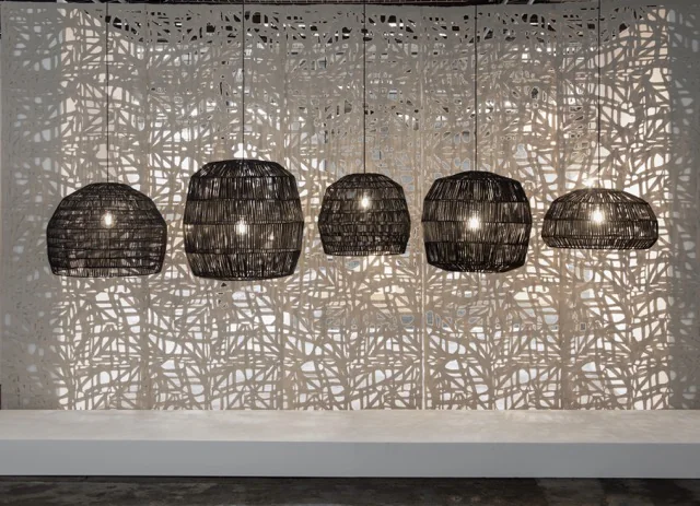 Fünf schwarze NAMA ay illuminate Lampen in verschiedenen Größen hängen vor einer kunstvoll gemusterten Wand und schaffen eine stimmungsvolle Atmosphäre.