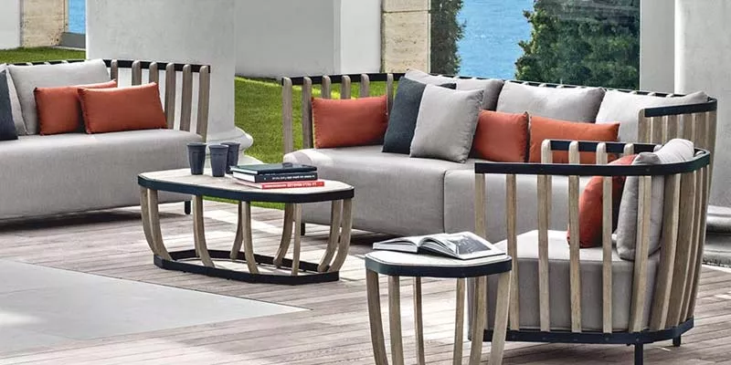 Ethimo Swing Outdoor Loungegruppe in Grau mit orangefarbenen Kissen auf Holzterrasse vor Meerblick, stimmungsvolles Ambiente.