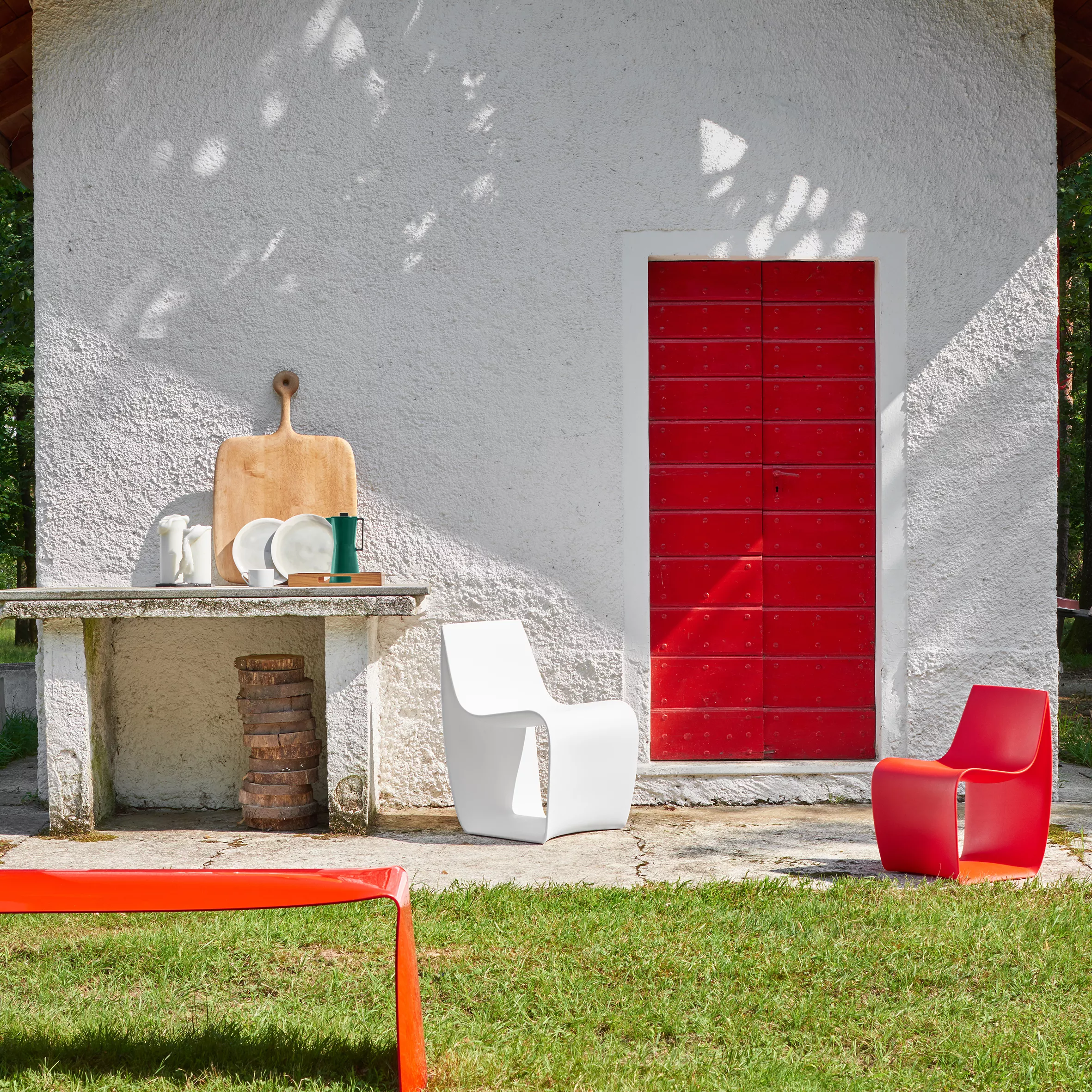 MDF Italia Sign Matt Stuhl in Weiß und Rot vor einem weißen Gebäude mit roter Tür und einem Tisch mit Geschirr im Freien