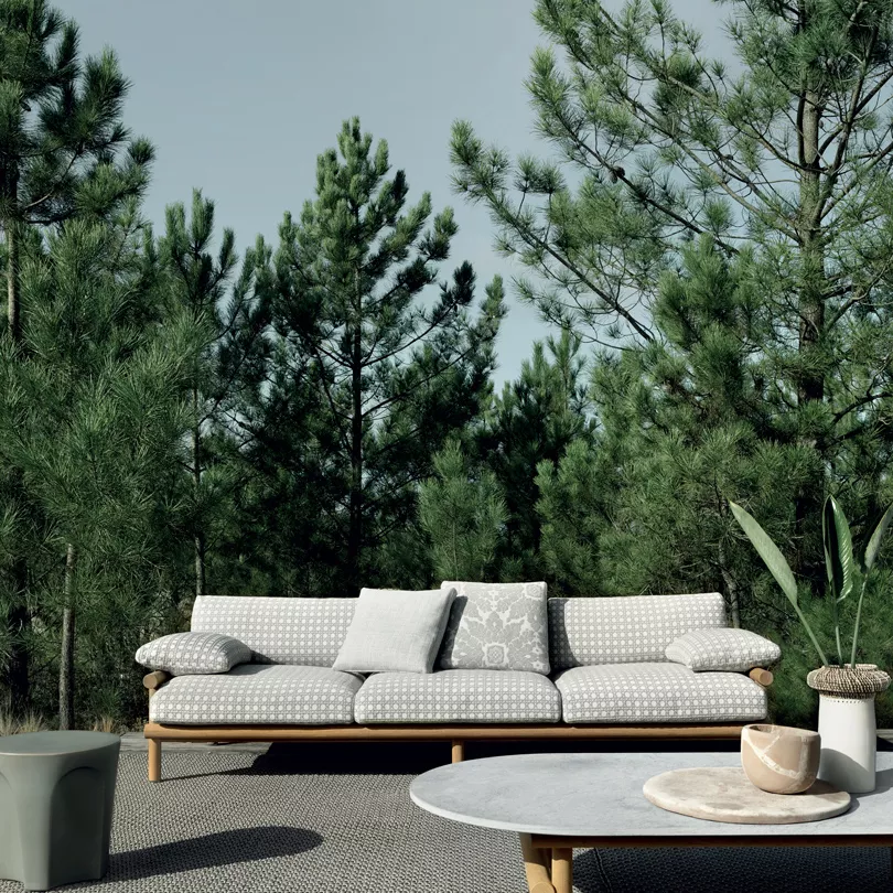 B&B Italia Ayana Gartensofa I 3-er Sofa in einem Garten mit Kissen auf einem Teppich vor Bäumen und einem Tisch mit Pflanzen und Dekoration