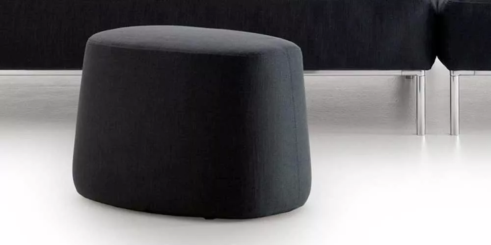 BeB Italia Frank Hocker in schwarzem Stoff vor einem schwarzen Sofa auf weißem Boden ohne Hintergrund