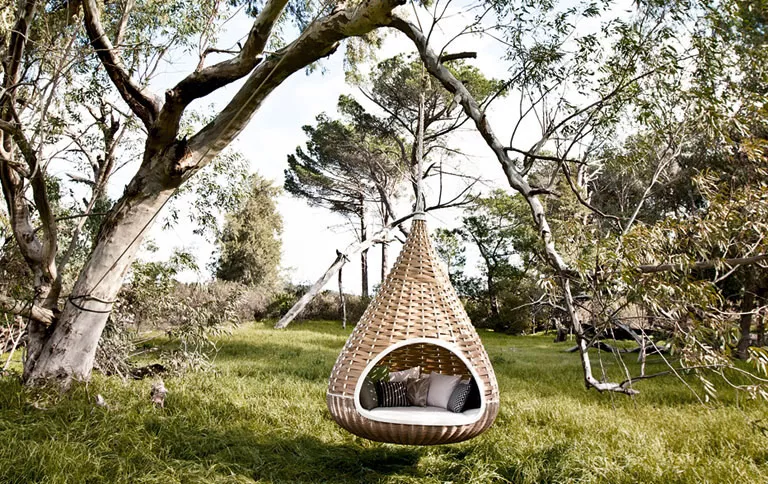Nestrest Hanging Lounger rund 200 cm von Dedon hängt an einem Baum in einem grünen Wald mit Kissen im Inneren