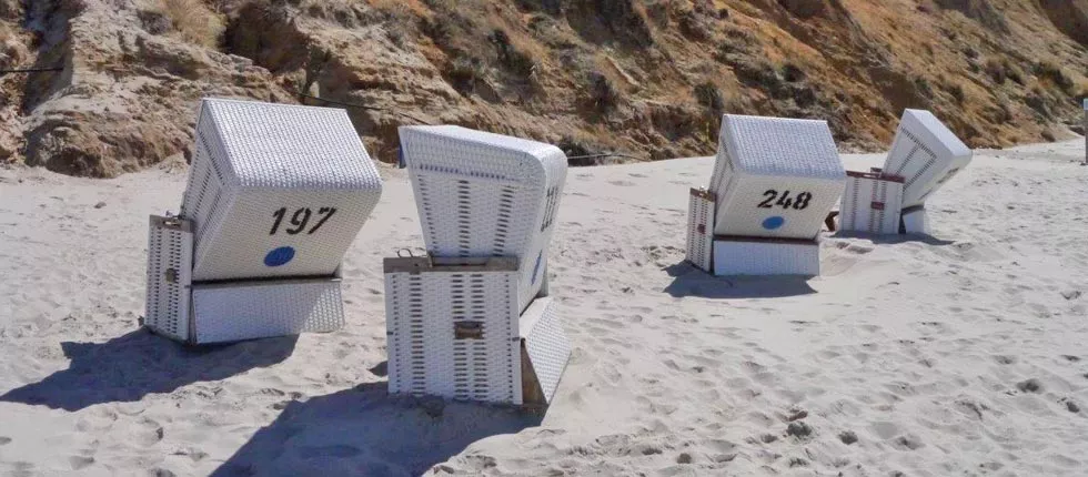 Strandkörbe in Weiß am Sandstrand vor einer Felswand, nummeriert mit 197 und 248, bei sonnigem Wetter.